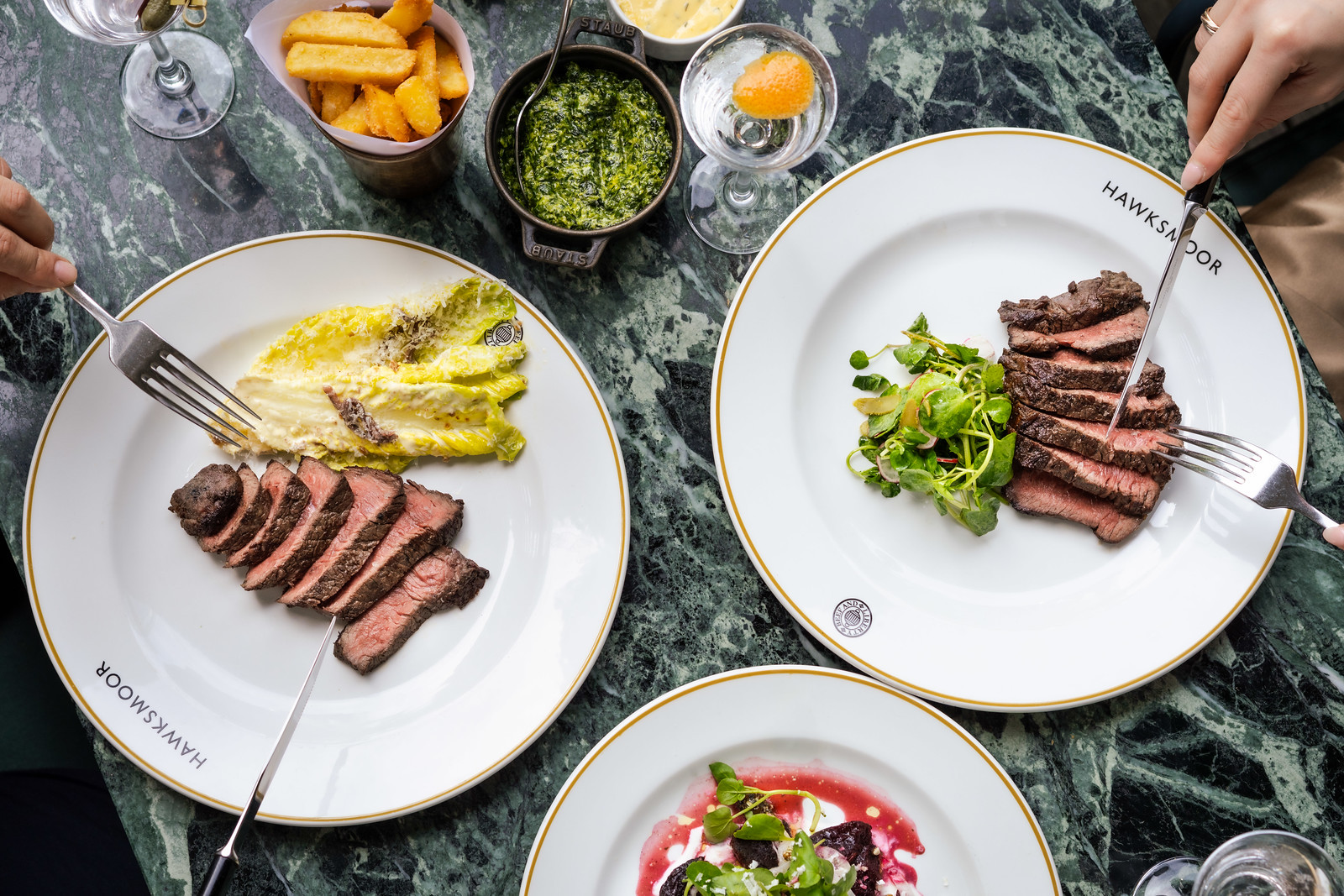 Overhead view of steak slices with salad and fries on white plates at a marble table.