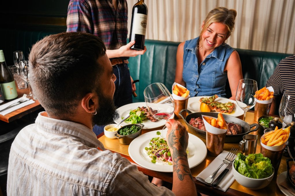 A group of diners sharing steak, fries, salads, and wine at a restaurant table.