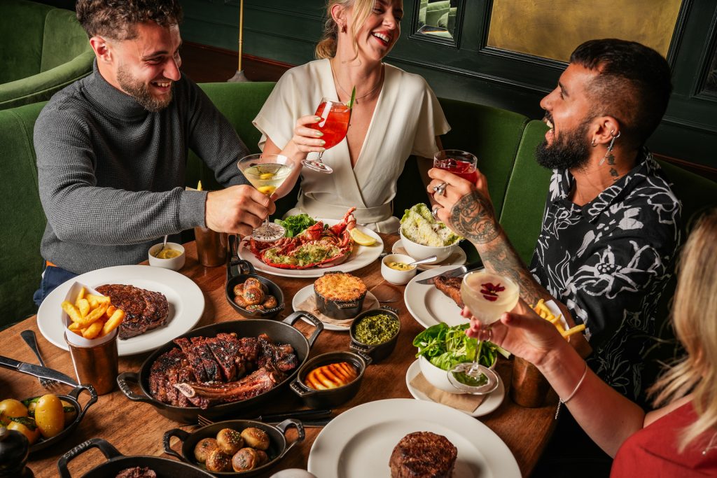 Graduations at Hawksmoor Dublin 1 A group of 3 friends around the table of steaks and sides, raising glasses